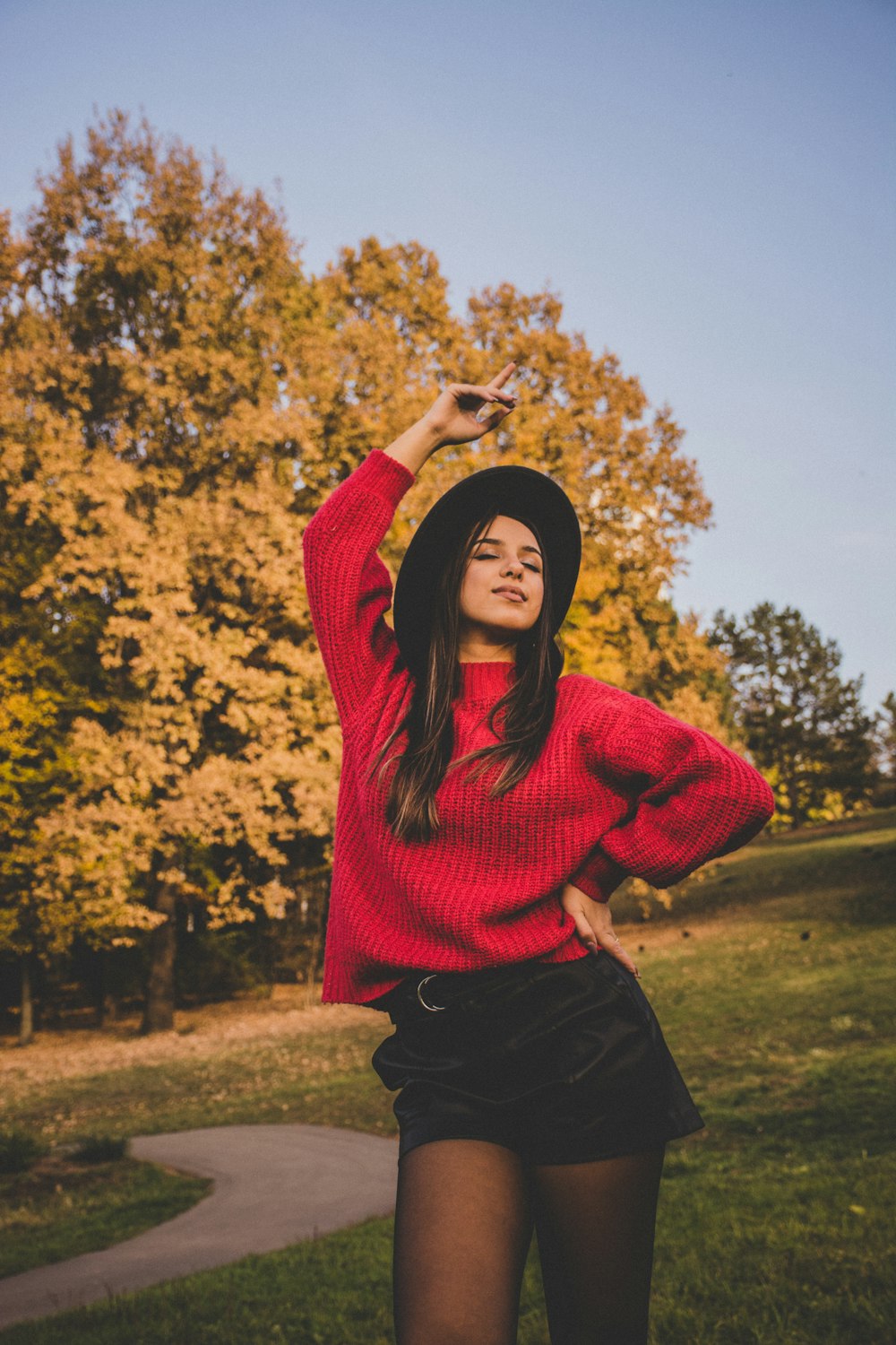 woman in red sweater standing on grass near trees during daytime