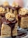 Layered dessert pieces topped with a glossy chocolate sauce, adorned with piped cream decorations. The dessert consists of multiple light-colored layers sandwiched with a creamy filling.