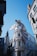 A fantasy setting features a large dragon perched atop Gringotts Bank with its mouth open, positioned among tall buildings under a clear blue sky. The dragon's wings are spread, adding a dramatic flair to the street scene.