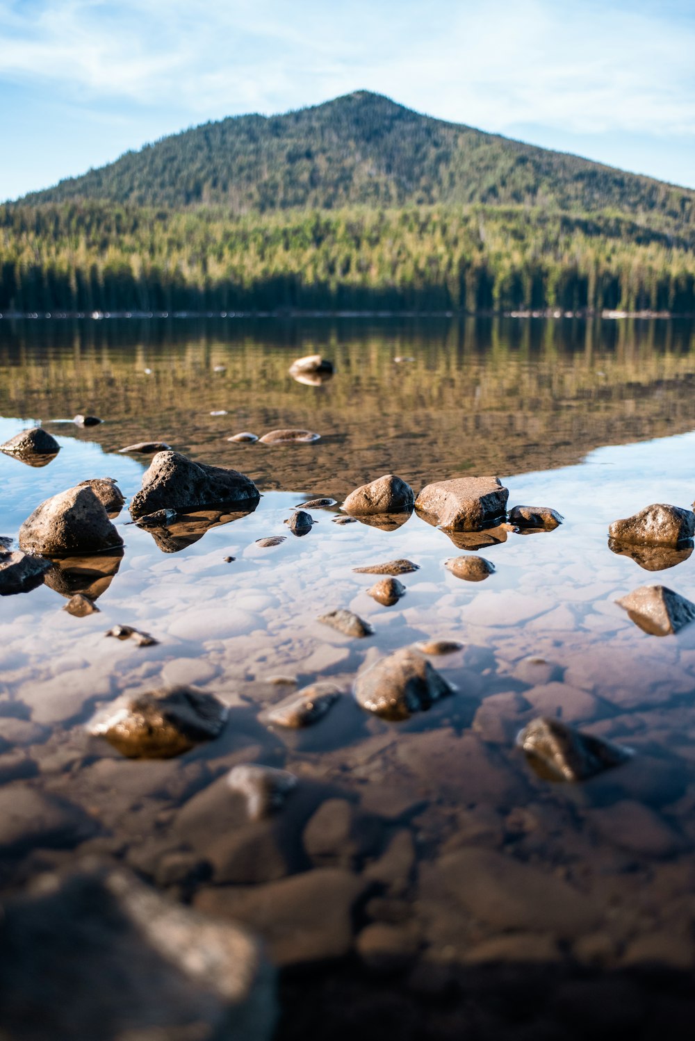 brown rocks on body of water viewing mountain under white and blue sky during daytime