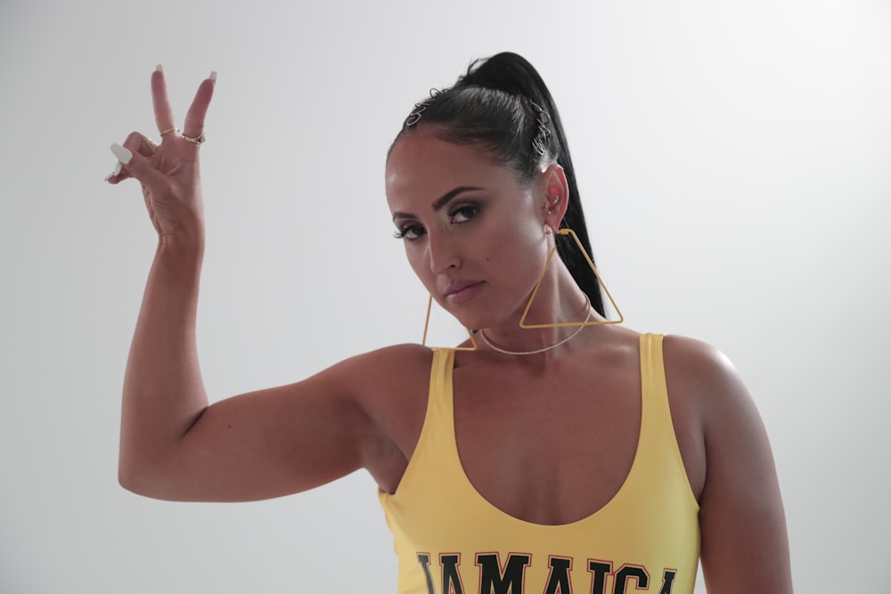 woman wearing yellow and black tank top standing while making peace hand sign