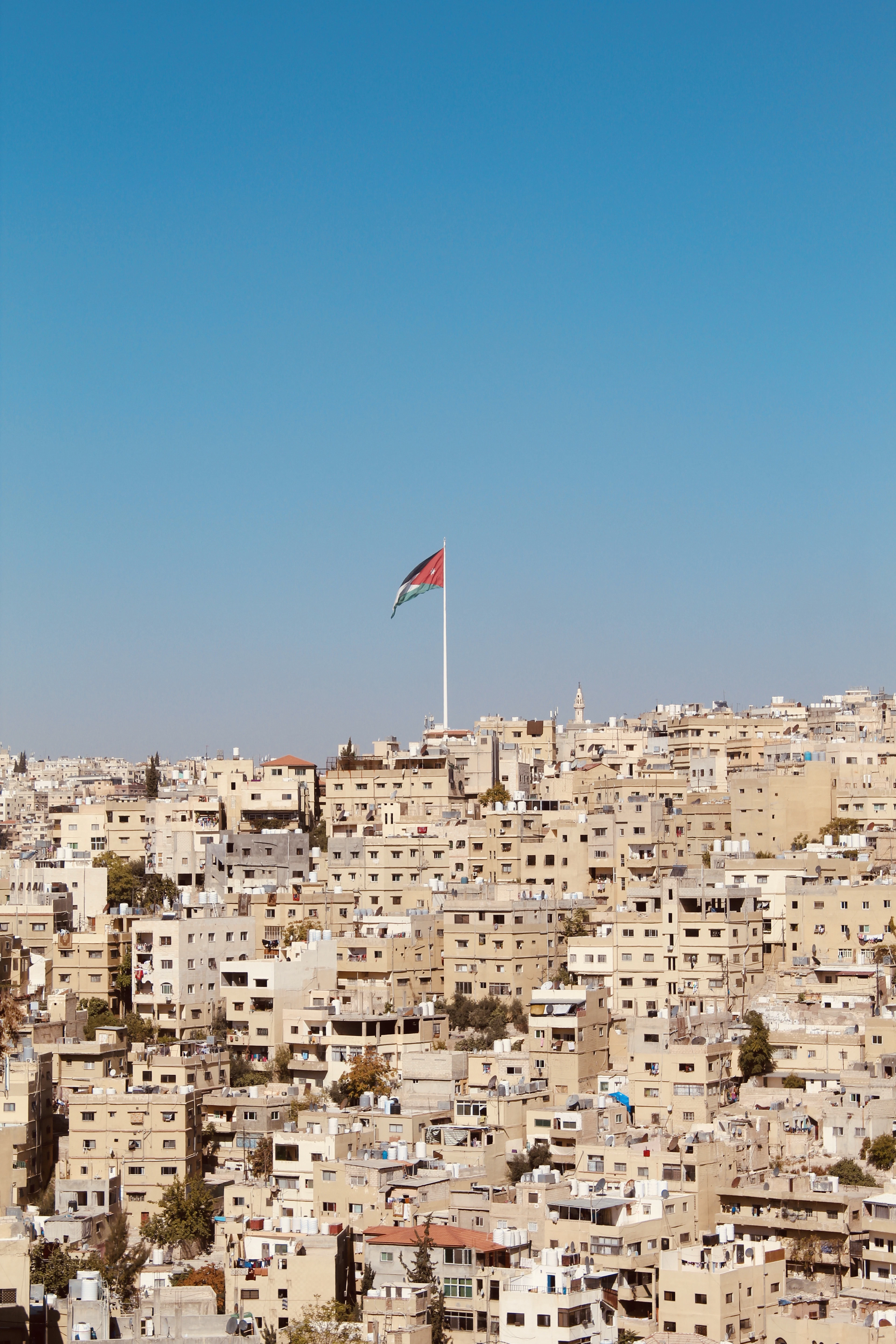 The Jordanian flag flies above a dense hillside of cream and beige homes in Amman.