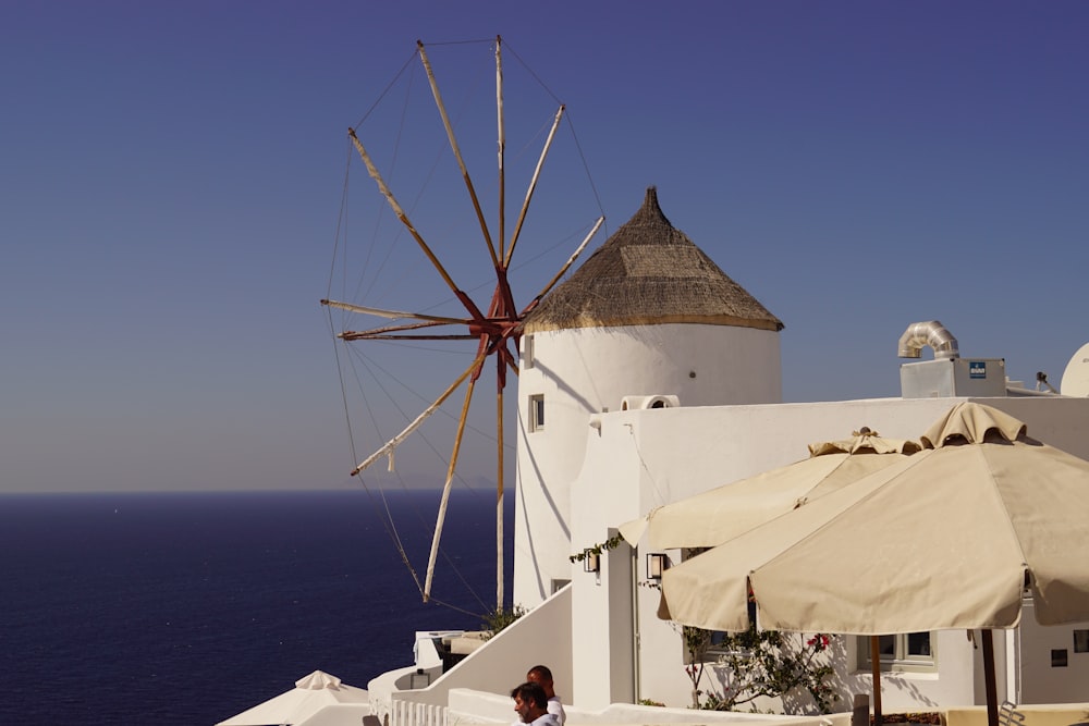 two people near white and brown windmill viewing blue sea during daytime