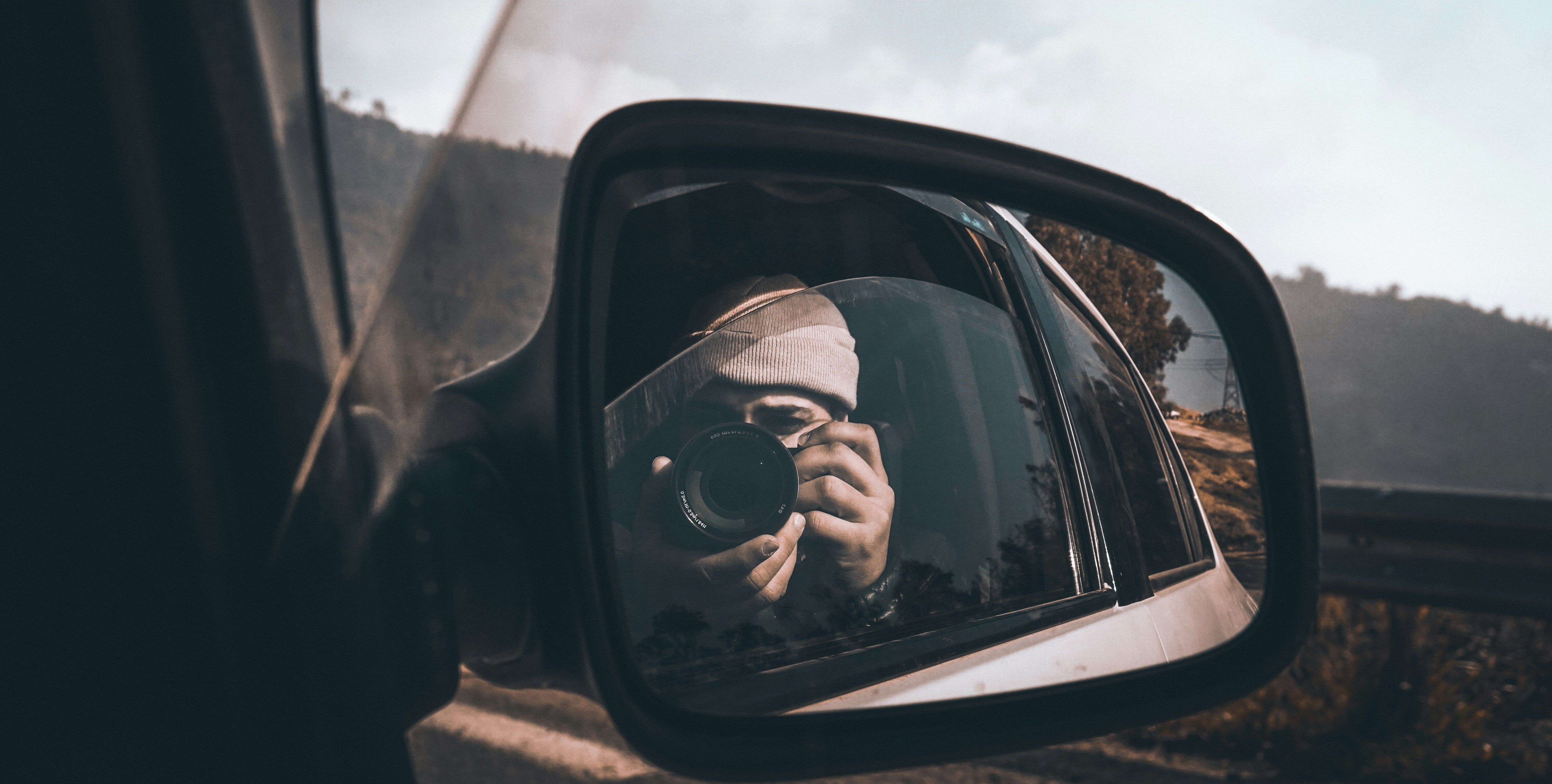 woman taking photo in front of vehicle side mirror
