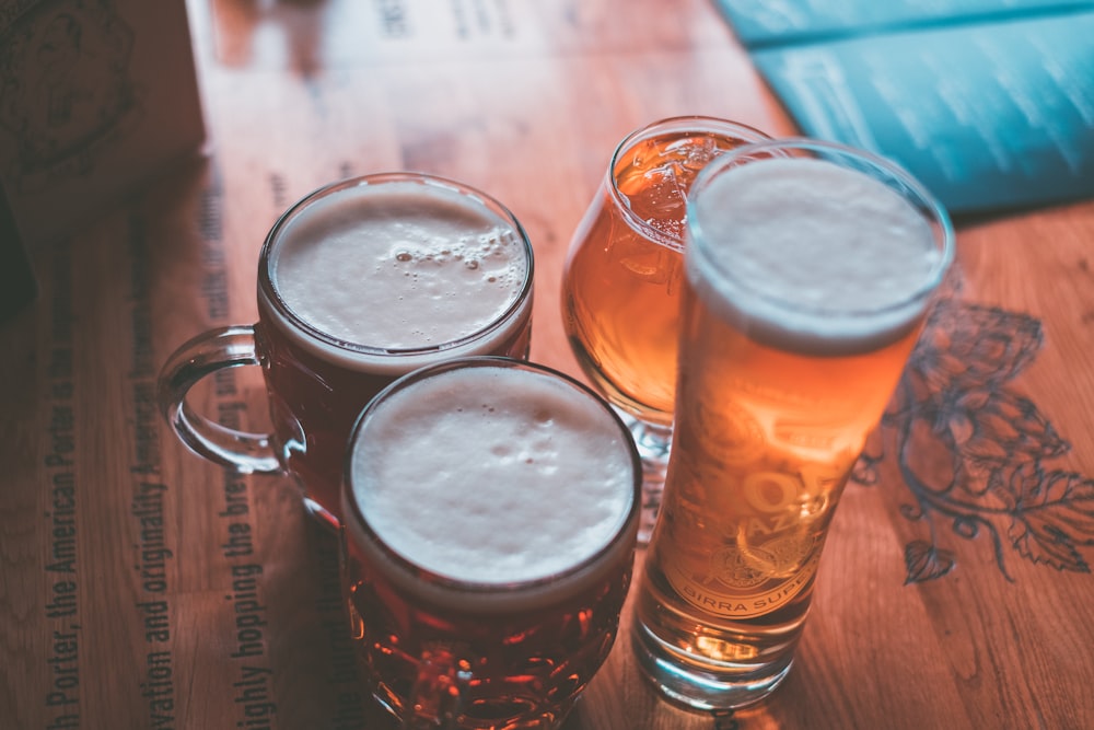 Taza de vidrio transparente y lata de cerveza sobre mesa de madera marrón