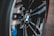 Close-up view of a car wheel featuring a BMW logo prominently displayed at the center, surrounded by sleek, shiny black spokes and hints of blue components in the background.