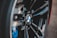 Close-up view of a car wheel featuring a BMW logo prominently displayed at the center, surrounded by sleek, shiny black spokes and hints of blue components in the background.