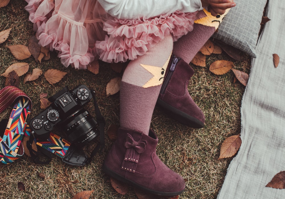 person's feet wearing pair of purple suede ankle boots beside black DSLR camera