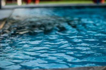 Close-up of a pool technician adjusting water chemicals beside a bright blue pool.