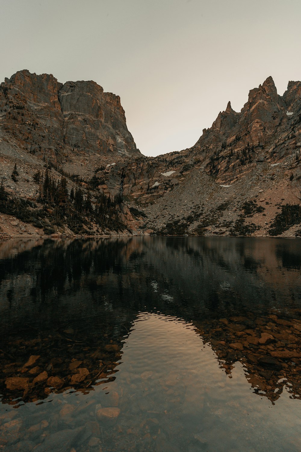 Fotografía de paisaje de cadenas montañosas marrones y negras detrás de un cuerpo de agua