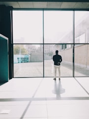 A young professional standing by a window, gazing outside with a hopeful expression in a minimalist office space.