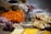 A beautifully arranged charcuterie board featuring sliced bread, assorted cheeses, cured meats, pistachios, grapes, and carrots. In the center sits a decorative small glass jar with delicate white flowers, next to an empty mason jar placed on a rustic wooden base.