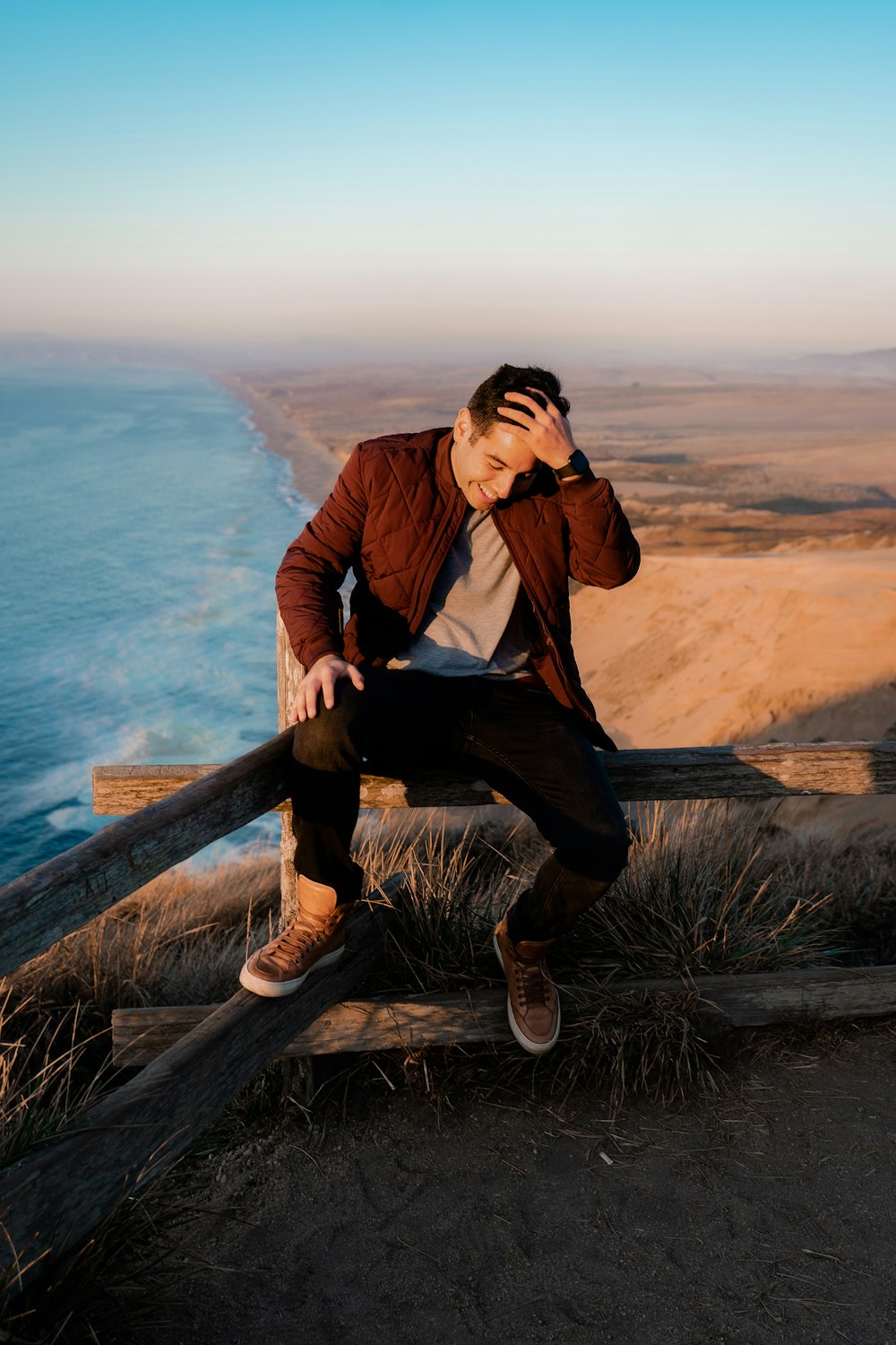 man wearing brown jacket sitting beside fence