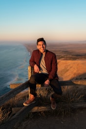 man sits on wooden fence in mountain peek during daytime