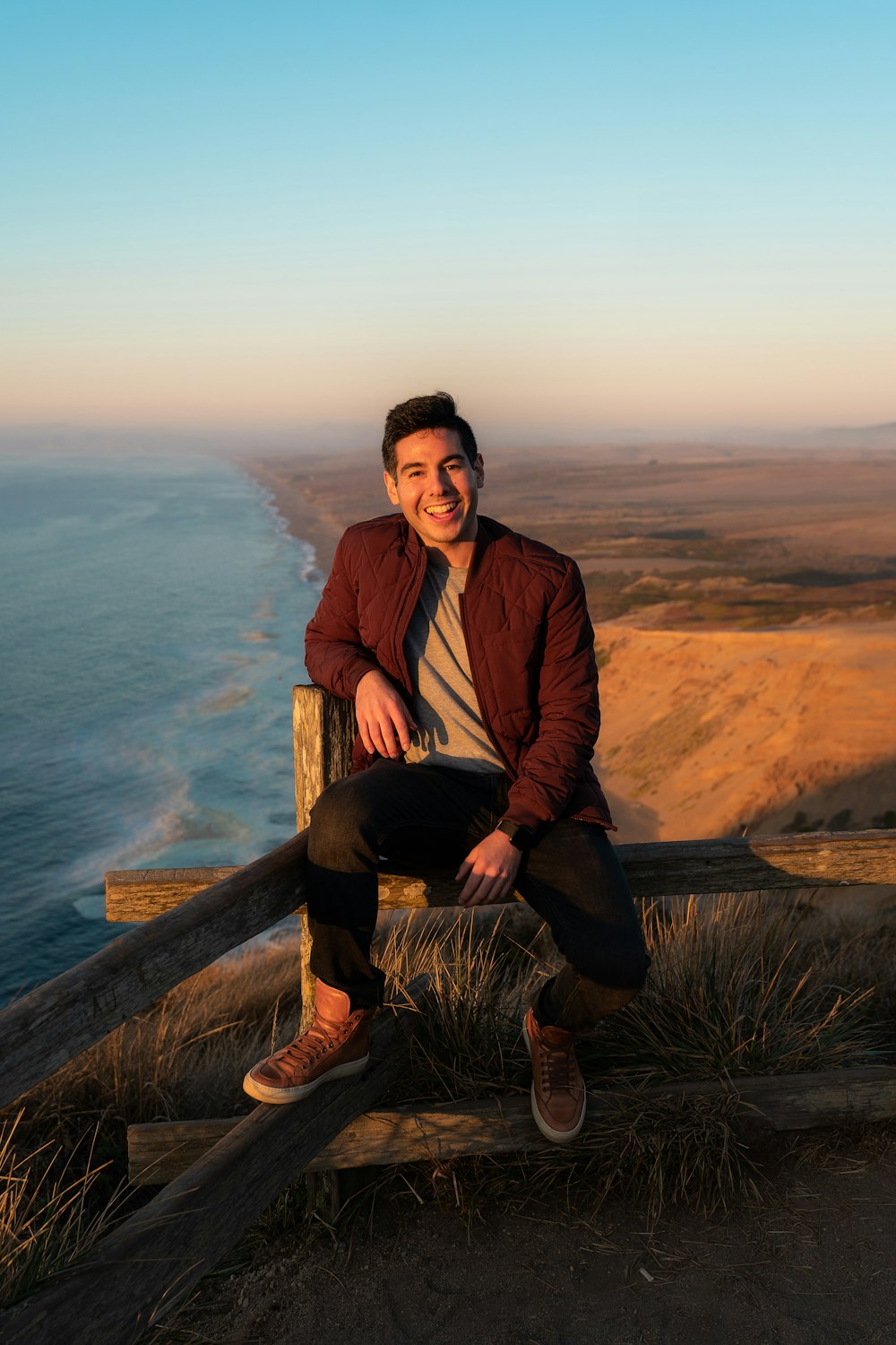 man sits on wooden fence in mountain peek during daytime