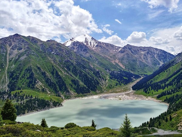 دریاچه‌ی شیری‌رنگ کوهستانی میان دامنه‌های سبز و قله‌ی برفی زیر آسمان ابری