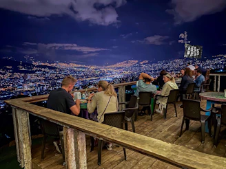 Guests enjoying a luxurious dinner on a terrace overlooking the sparkling city lights at night.
