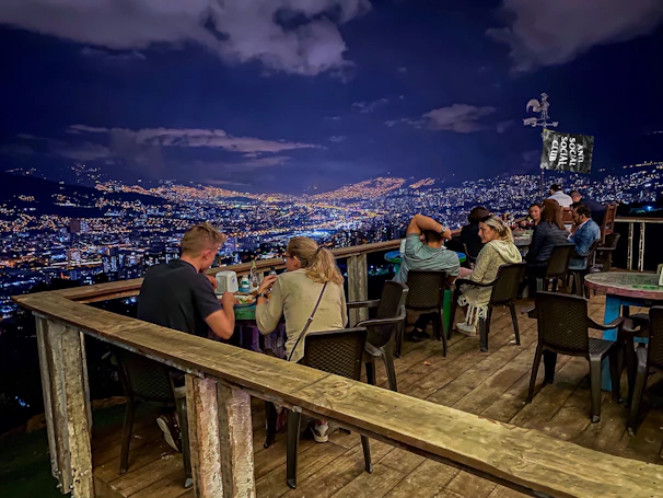 Guests enjoying a luxurious dinner on a terrace overlooking the sparkling city lights at night.