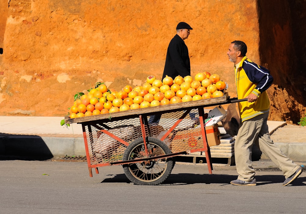 Mann schiebt Karren mit Orangen oben drauf