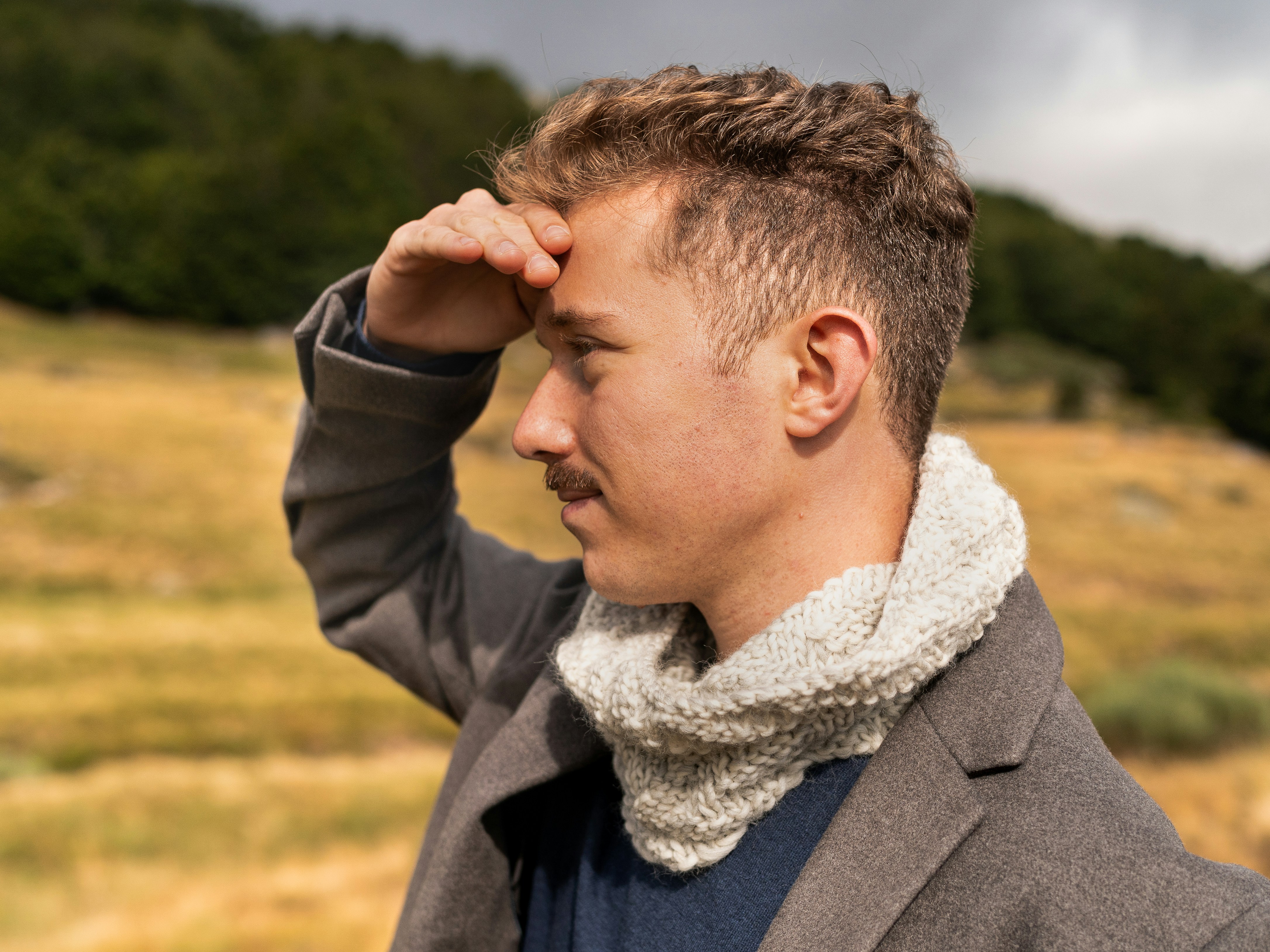 man wearing gray notched lapel suit jacket putting right hand on his forehead scarf teams background