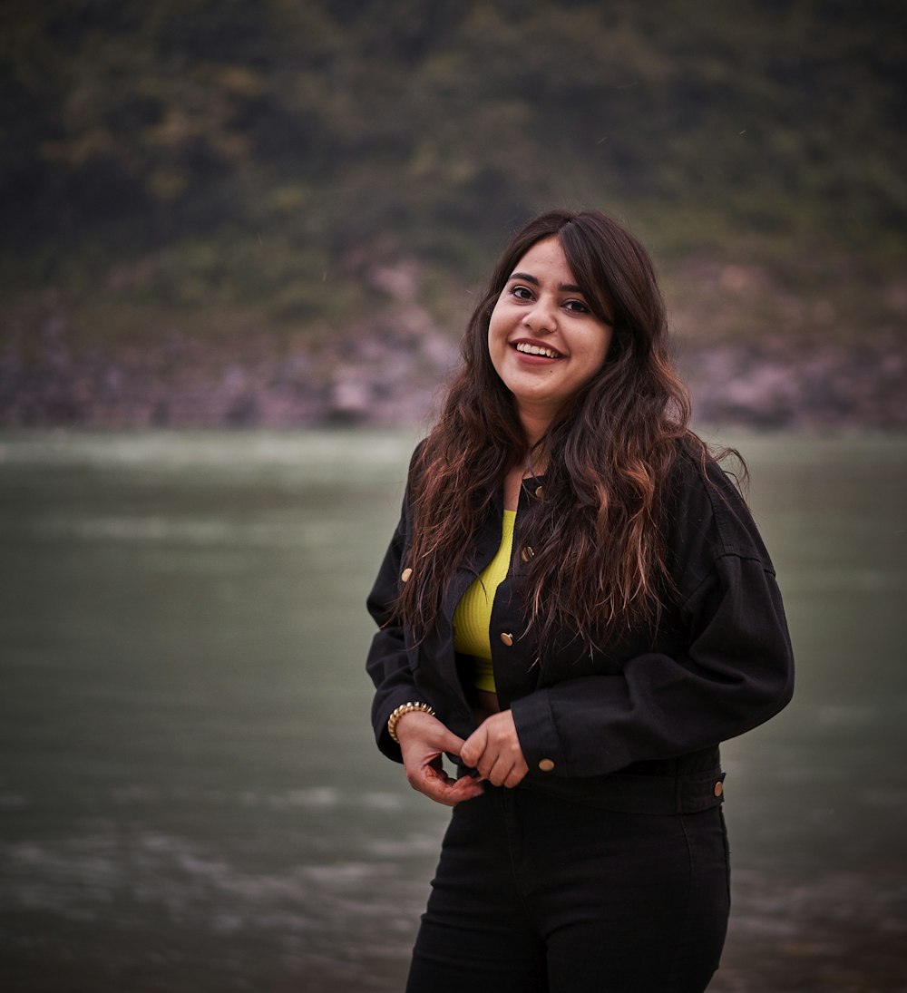 woman wearing black blazer standing and smiling near body of water