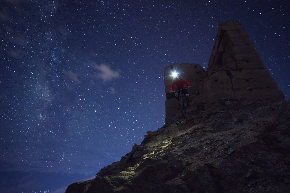 man riding on bicycle with headlamp on head on rock formation