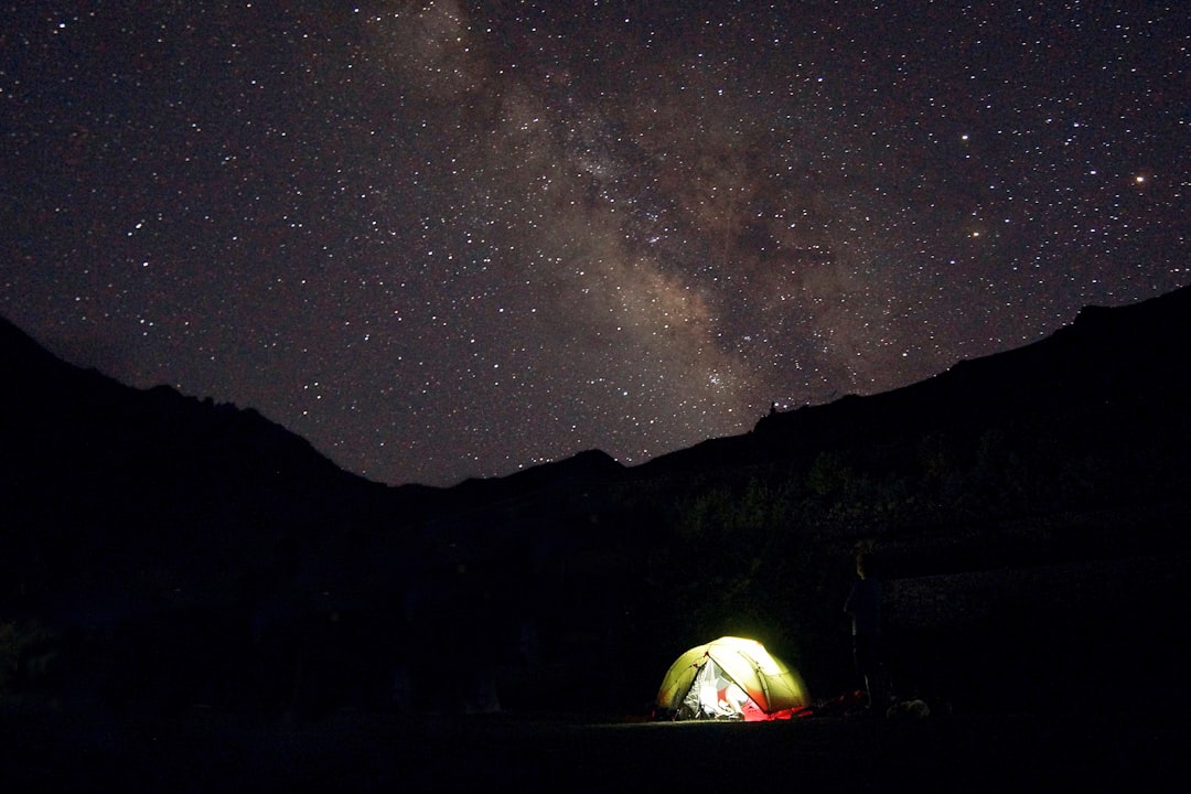 green tent with turned-on light in front of silhouette of mountain under the galaxy