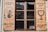 Wooden window shutters with signs and illustrations painted in black. The left shutter features a mermaid holding a glass, with text in a foreign language, while the right shutter displays a large wine glass icon and more text.