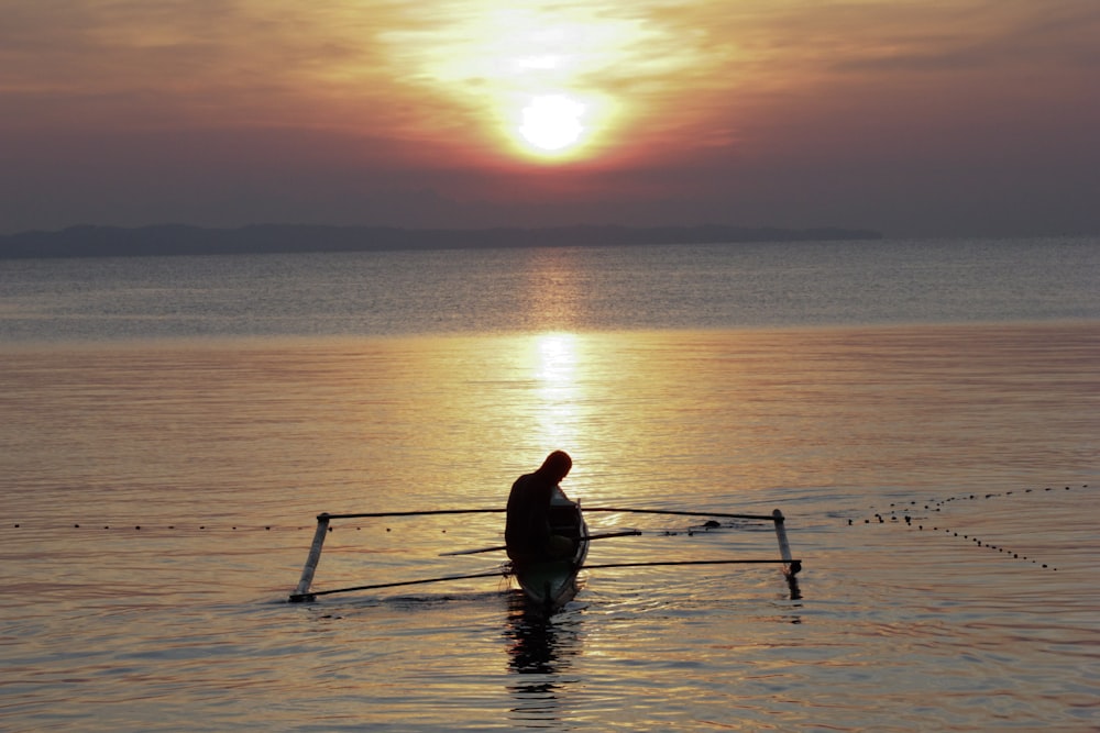 silueta de hombre montando barco en un cuerpo de agua tranquilo