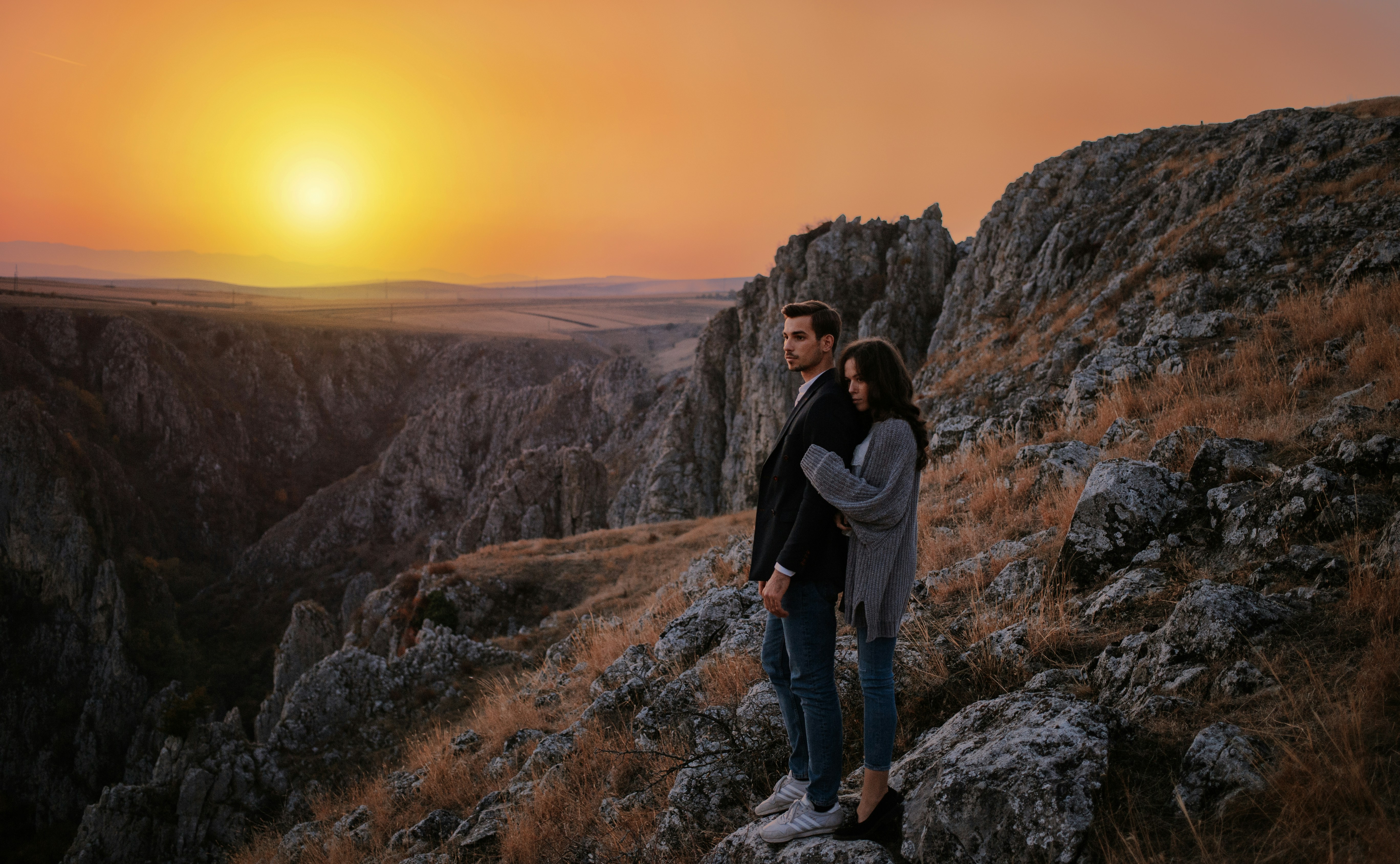 man and woman standing on boulder during golden hour