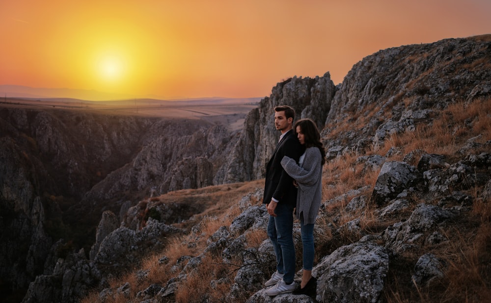 man and woman standing on boulder during golden hour