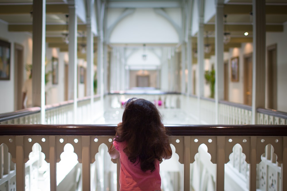 selective focus photo of girl standing on the white and brown wooden balustrade