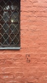 A textured orange brick wall features a window with an ornate metal grille on the left side. Black lettering reading 'ГК 2,5' with a downward arrow is visible on the brickwork.