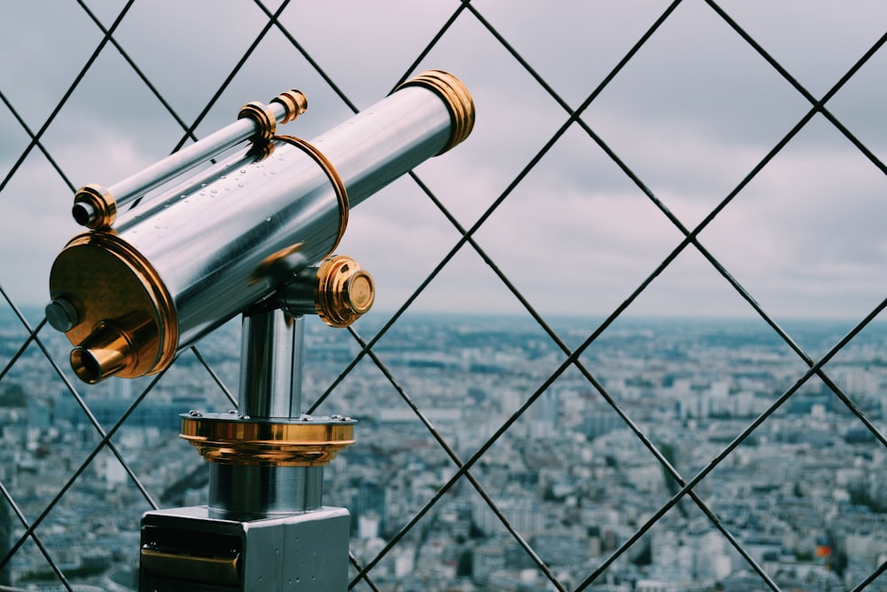 gray and gold telescope behind of cyclone fence