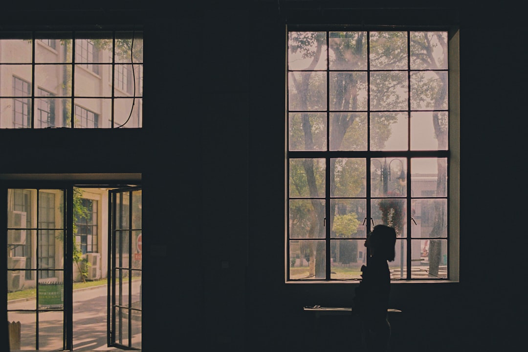 person standing while facing right side inside building showing open door surrounded with tall and green trees