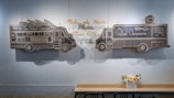 Black chalkboard drawings depict two food trucks with the words 'The Grilled Cheeserie' on a light blue wall. Above the trucks is a yellow cursive text that reads 'Melting the Hearts of Music City.' Below the wall, a wooden table with black chairs is adorned with a small vase of flowers.