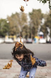 A cartoon girl named Belab playing joyfully under a large oak tree with autumn leaves around.