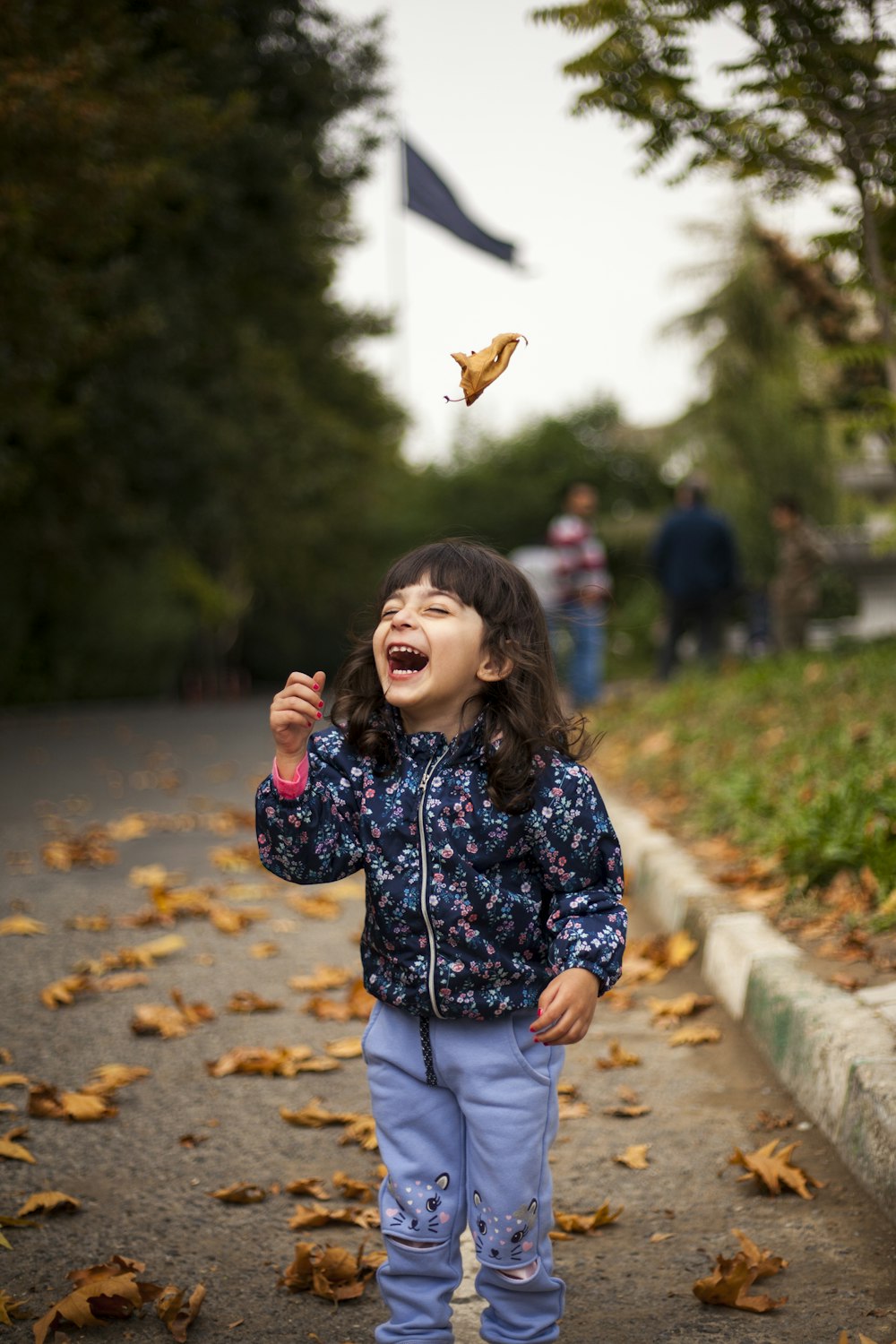 girl wearing blue and pink floral jacket standing on road laughing during daytime