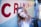 A person stands in a narrow hallway, leaning against a wall with the word 'CRIMINAL' painted in large red letters. The individual is wearing a black leather jacket and has long hair. The setting has a cool, urban vibe with blue and teal tones.