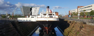 A historic ship docked at Passage West harbor with museum visitors nearby.