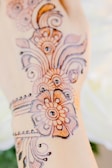 Intricate henna designs are displayed on a hand. The patterns consist of floral and circular motifs, crafted in a detailed style with fine lines and curves, typically associated with traditional henna art.