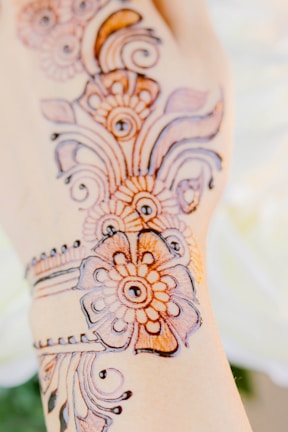 Intricate henna designs are displayed on a hand. The patterns consist of floral and circular motifs, crafted in a detailed style with fine lines and curves, typically associated with traditional henna art.