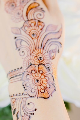 Intricate henna designs are displayed on a hand. The patterns consist of floral and circular motifs, crafted in a detailed style with fine lines and curves, typically associated with traditional henna art.