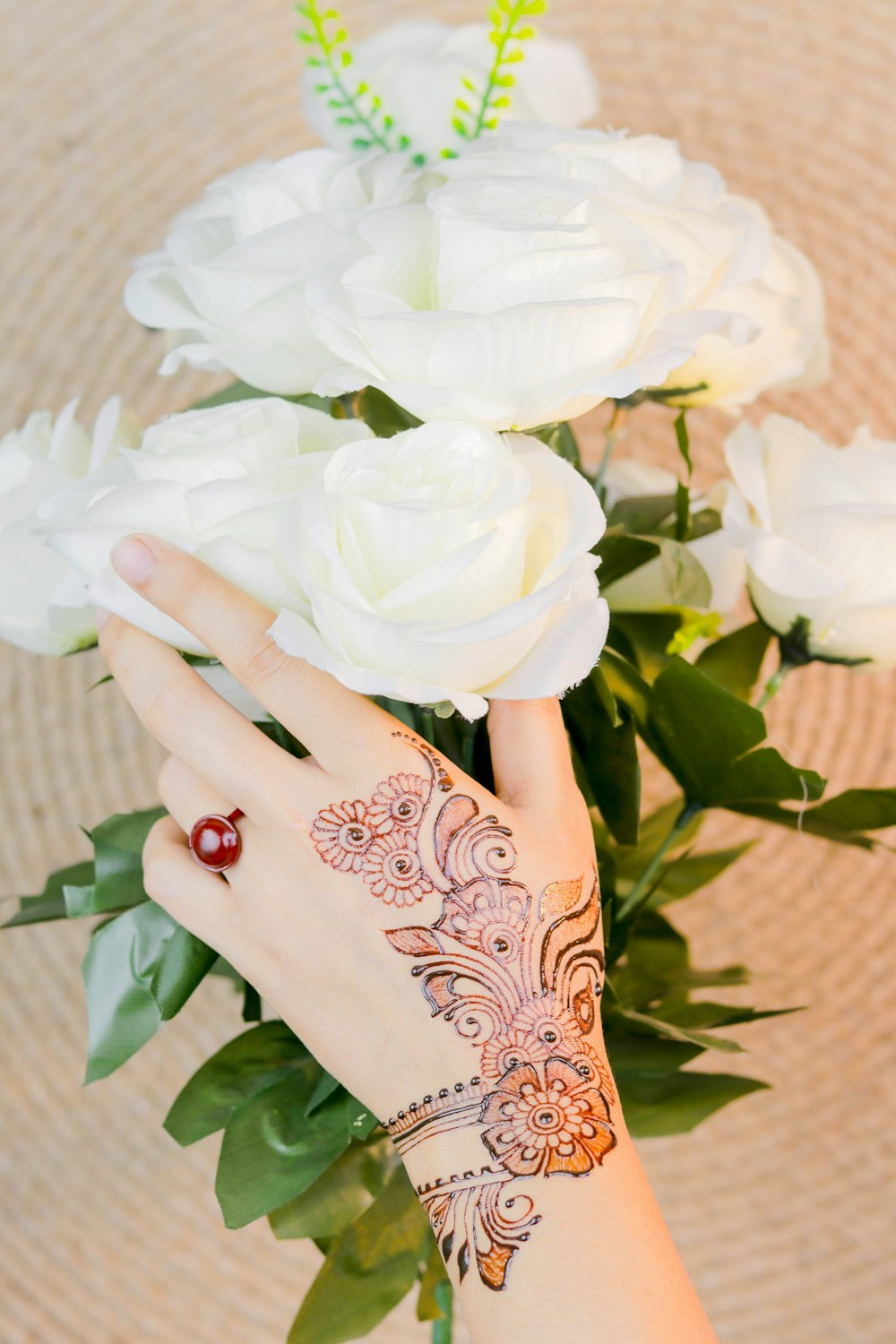 Personne avec un tatouage mehndi brun tenant des fleurs roses blanches