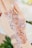 A hand adorned with intricate henna designs featuring floral patterns and swirls. The artwork is detailed and appears freshly applied. Subtle shadows and highlights accentuate the patterns, with a soft focus on the background, suggesting a setting with flowers.