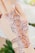 A hand adorned with intricate henna designs featuring floral patterns and swirls. The artwork is detailed and appears freshly applied. Subtle shadows and highlights accentuate the patterns, with a soft focus on the background, suggesting a setting with flowers.