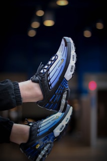 A pair of athletic shoes with a vibrant blue and black design, highlighted by prominent air cushions and sleek lines. The shoes feature a modern and stylish appearance with intricate detailing on the sides and soles.