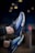 A pair of athletic shoes with a vibrant blue and black design, highlighted by prominent air cushions and sleek lines. The shoes feature a modern and stylish appearance with intricate detailing on the sides and soles.