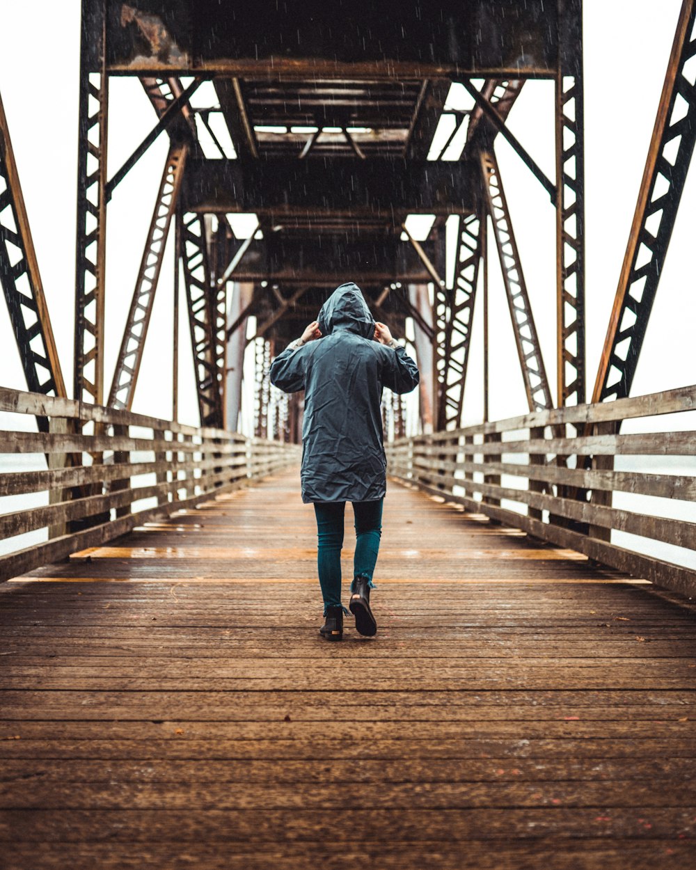 person wearin blue jacket walking on wooden bridge