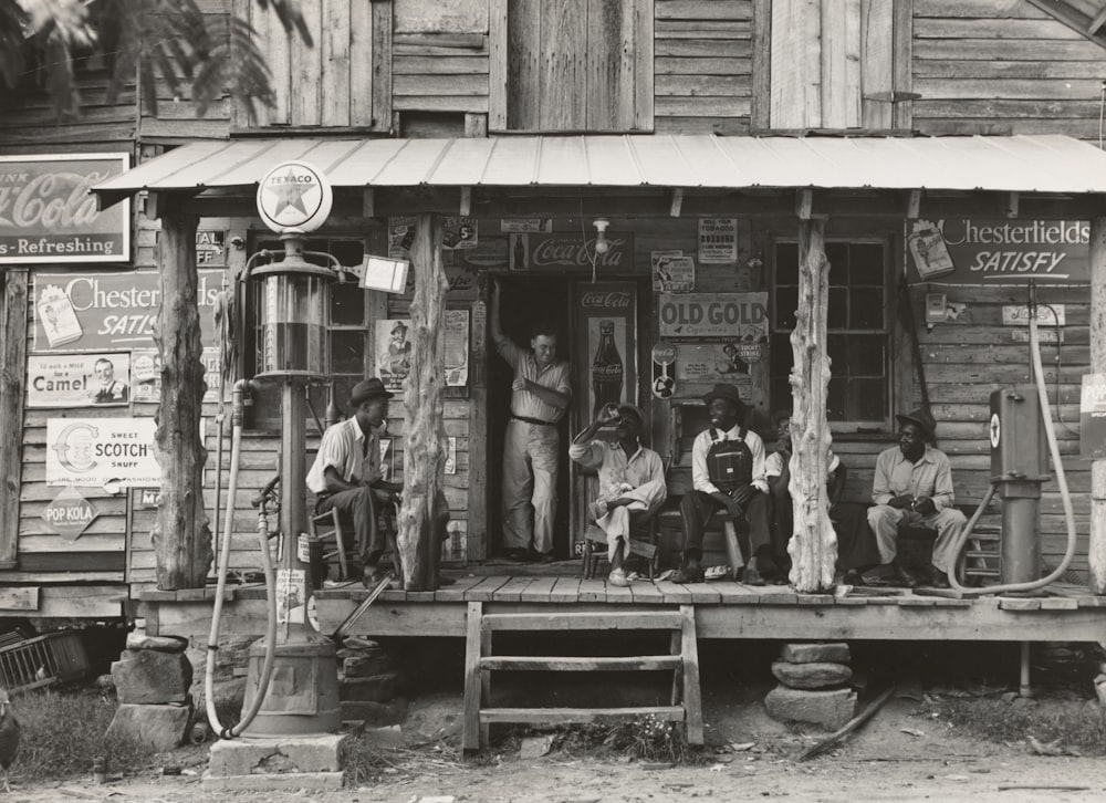men sitting and standing on house porch near gas dispenser during day